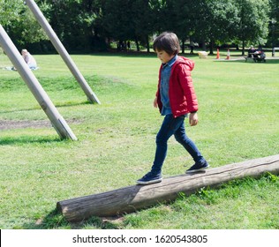 Side View Kid Walking On Wooden Climbing In The Park, Child Enjoying Activity In A Climbing Adventure Park On Summer Sunny Day, Selective Focus Of Child Sitting On Balance Beam Playground.