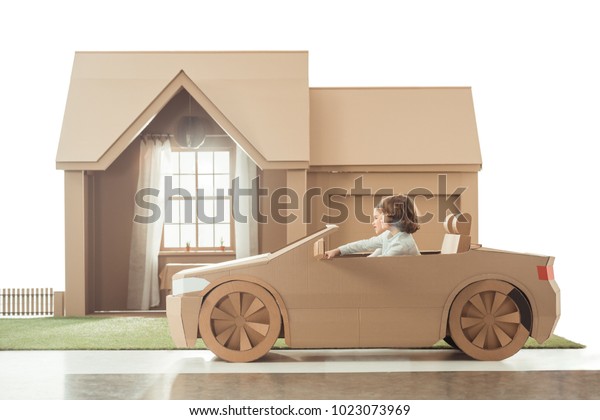 side view of kids riding cardboard car in front of\
house isolated on white
