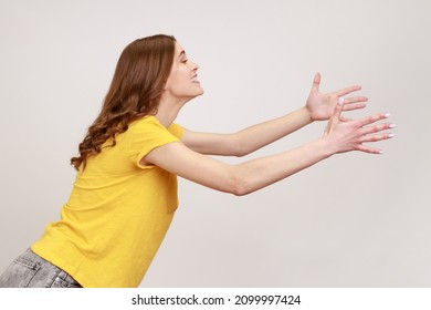 Side view of kind young female with brown hair outstretching hands as if giving for free, offering to embrace, complacency and egoism concept. Indoor studio shot isolated on gray background. - Shutterstock ID 2099997424