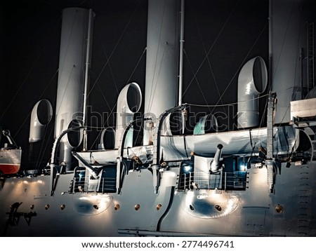Side view of a large ship's superstructure and funnels against a dark sky. A dramatic, low-angle shot capturing the massive, curved funnels and superstructure of a large passenger or cruise ship. The