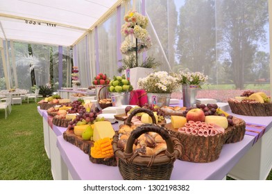 Side View Of A Lavish Wedding Buffet Table Filled With Fruits, Bread, Sliced Meats And Cheeses.