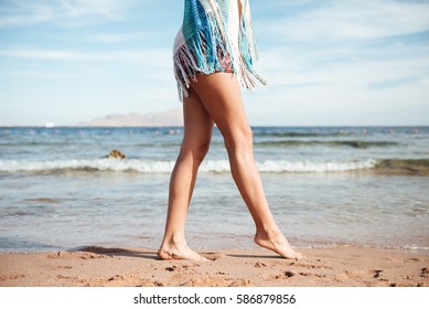 Side View Of Legs Of Woman Which Walking On The Beach Near The Sea. Cropped Image