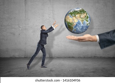 Side view of little businessman reaching out for planet Earth that is levitated above big man's hand emerging from right. Collaboration. Global industry. Industry uses Earth's resources to the full. - Shutterstock ID 1416104936