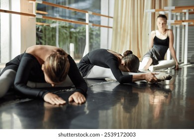 Side view of little female ballet dancer stretching muscles bending over legs while warming up on studio floor preparing for group class, copy space - Powered by Shutterstock