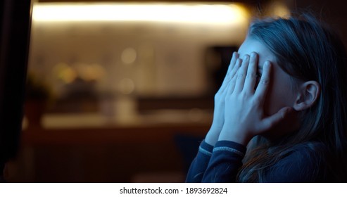 Side View Of Little Girl Watching Scary Movie At Home On Tv At Home. Cute Preschool Kid Sitting Near Large Tv Screen And Covering Face With Hands Watching Horror Movie