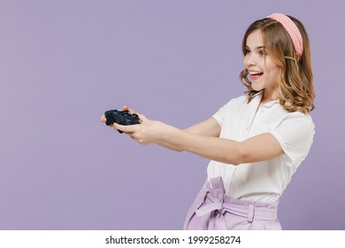 Side View Of Little Joyful Happy Smiling Kid Girl 12-13 Years Old In White Shirt Play Pc Game With Joystick Console Isolated On Purple Background Children Studio Portrait Childhood Lifestyle Concept