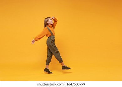 Side view of little kid girl 12-13 years old in turtleneck, jumpsuit isolated on yellow background. Childhood lifestyle concept. Mock up copy space. Holding hand at forehead looking far away distance