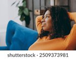 Side view little minded thoughtful kid teen girl wear casual clothes look aside sits on blue sofa couch stay at home hotel flat rest relax spend free spare time in living room indoor. Lounge concept