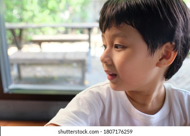 Side View Of Little Toddler Boy With Short Hair In White T-shirt Smiling And Looking To Side. Portrait Of Cheerful Asian Boy With Positive Emotion. Kids Interest Concept. Natural Light & Shadow Shot.