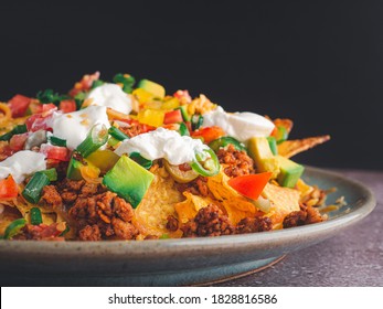 Side view of loaded minced pork nachos on plate with black wall background. Space for text. Concept of Mexican food
