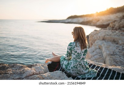 Side view of lone woman sitting on rocky beach