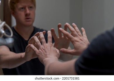 Side View Of Lonely And Sad Caucasian Man Wearing Black T-shirt And Reaching Out To His Reflection In The Mirror. Selective Focus. Blurred Face. Mental Health Theme.