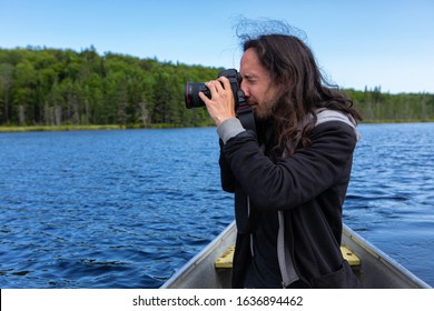 Side View Of Long Haired Native American Young Man Riding In Canoe In Lake While Shooting Scenic Landscape In Northern Quebec, Canada