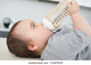 Side View Of Lovely Baby Boy Drinking Milk While Lying On Kitchen Counter