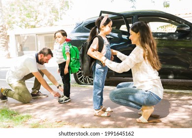 Side View Of Loving Young Parents Smiling And Saying Goodbye To Their Little Kids Before Sending Them To School In The Morning 