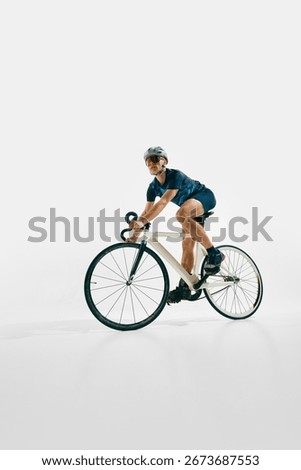 Side view low angle image of focused man, professional cyclist in full gear, riding bike, training isolated on white background. Concept of sport, competition, active lifestyle, endurance