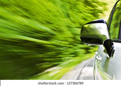 Side View Of A Luxury Car Driving Fast On A Winding Road In The Woods