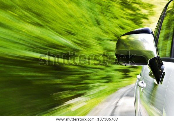 Side view of a luxury car driving fast on a winding\
road in the woods