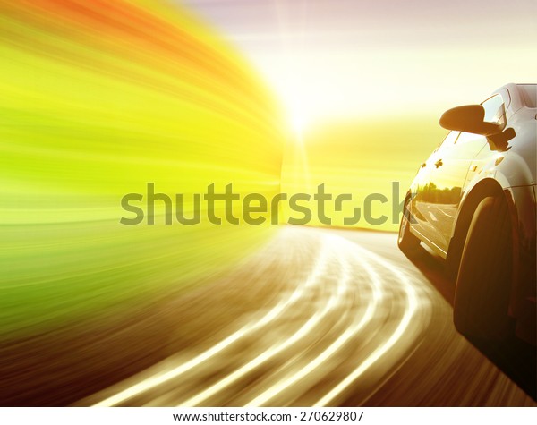 Side view of a luxury car driving fast on a winding\
road in the woods