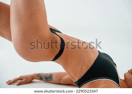 Side view. Lying down on the floor. Young caucasian woman with athletic body shape is indoors at daytime.