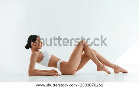 Side view, lying down. Young woman with slim body type is in fitness clothes in the studio.