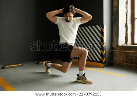 Side view of male athlete in active wear preparing for championship training his legs and full body muscles at gym, lunging forward, putting hands behind head, warming up before hard workout