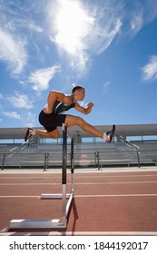Side view of a male athlete jumping over a hurdle in the race on running track - Shutterstock ID 1844192017