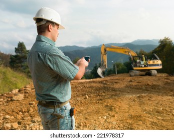 side view of male engineer standing on construction site holding mobile phone