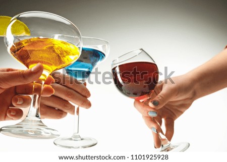 The side view of male and female hands with colorful exotic cocktails and fruits against white studio background. Toast, clinking glasses concept. Summer time concepts