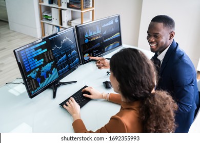 Side View Of Male And Female Stock Market Broker Analyzing Graphs On Laptop At Workplace