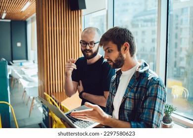 Side view of male freelancers in casual wear making publication in social media on portable computer and collaborating on project in modern workspace - Powered by Shutterstock