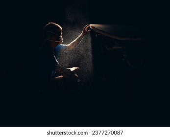 Side view of male master in respirator sitting on haunches in dark dusty garage and making surfboard under sunlight - Powered by Shutterstock