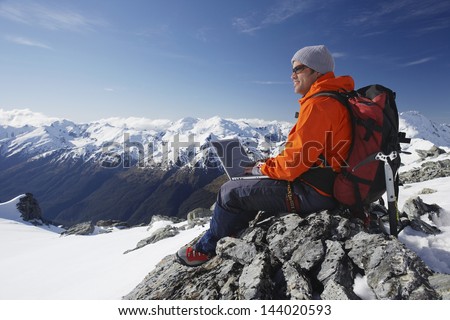 Side view of a male mountain climber using laptop on mountain peak