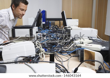 Side view of a male office worker looking at wire mess connecting computers and printers in office