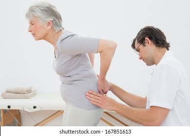 Side view of a male physiotherapist examining senior woman's back in the medical office - Powered by Shutterstock