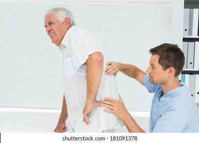 Side view of a male physiotherapist examining senior mans back in the medical office - Powered by Shutterstock