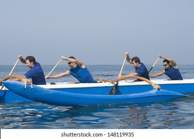 Side View Of Male Rowers Paddling Outrigger Canoe In Race