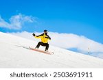 Side view male snowboarder wear yellow black on piste ski downhill fast motion in Alps. Active winter holidays, skiing downhill in overcast day. Ski rides on the track with swirls of fresh snow