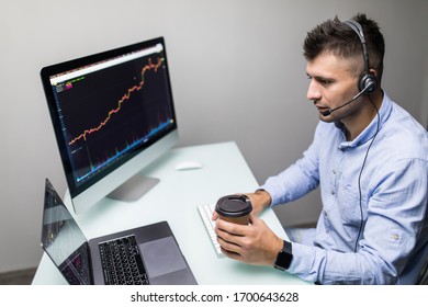 Side view of male trader using multiple computer screens while communicating through headphones at desk