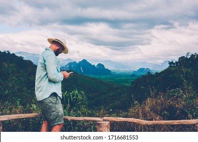 Seitenansicht des männlichen Reisenden, der das Handy in Händen hält, und Lesefunktion über Bewerbung während der Reise zum Nationalpark. Tourist Mann mit Smartphone im Freien. Online-Navigation mit Mobiltelefonen