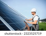 Side view of male worker installing solar modules and support structures of photovoltaic solar array. Electrician wearing safety helmet while working with solar panel. Concept of sun energy.