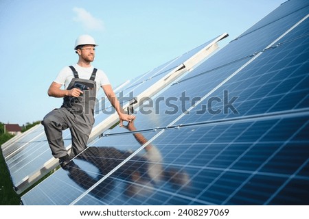 Side view of male worker installing solar modules and support structures of photovoltaic solar array. Electrician wearing safety helmet while working with solar panel. Concept of sun energy.