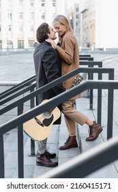 Side View Of Man With Acoustic Guitar Standing On Stairs Face To Face With Happy Woman