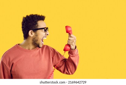 Side View Man With Angry Face Expression Shouting At Stupid Call Center Tech Support Service Line Helpdesk Operator. Scared Shocked Terrified Or Enraged Guy On Yellow Color Holding Old Phone Receiver