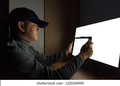 Side view of man Hacker, Thief sit at the computer monitor, white screen tablet in the dark room and low-light photo.