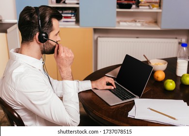 Side view of man in headset working on laptop near breakfast on table