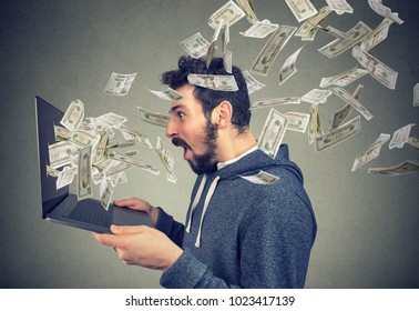Side view of man holding laptop and winning plenty of money in social media. 