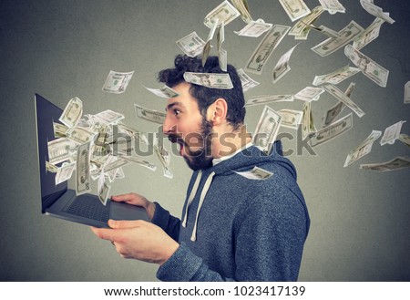 Side view of man holding laptop and winning plenty of money in social media. 