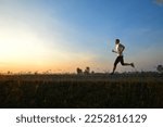 Side view of a man jogging on country road with sunrise background.