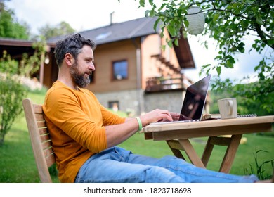 Side view of man with laptop working outdoors in garden, home office concept. - Shutterstock ID 1823718698